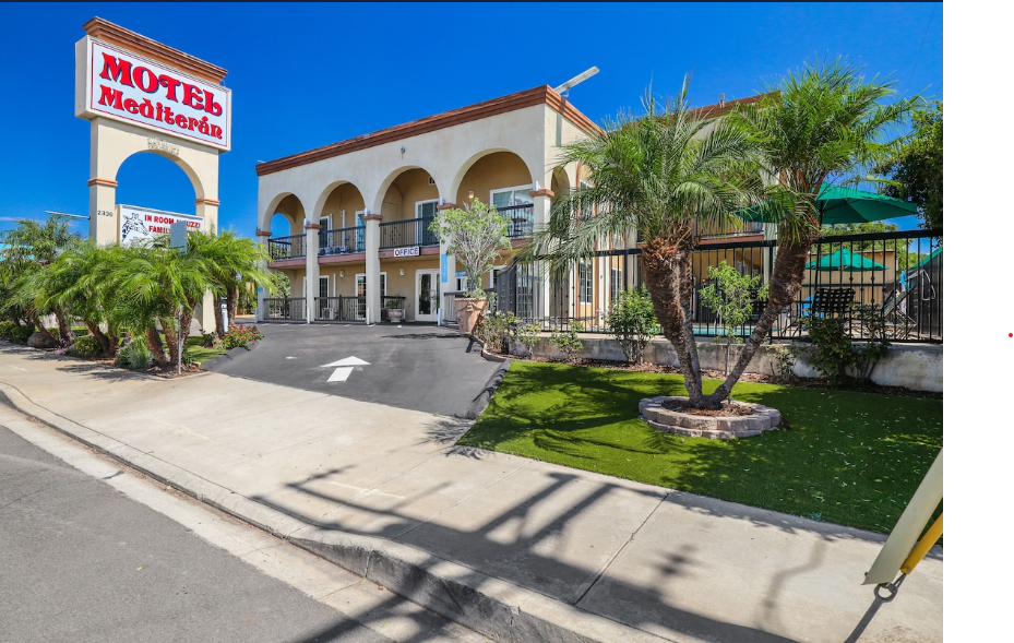 Roadside view of the motel sign and arched facade flanked by tall palm trees